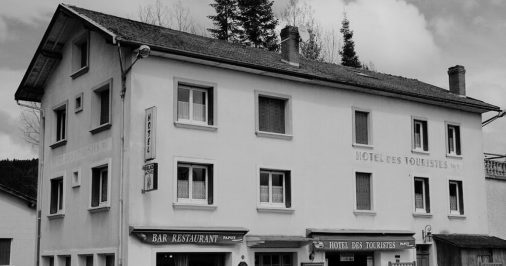 Photo en noir et blanc de la façade de l’Hôtel des Touristes à Vollore-Montagne, ancien hôtel-bar-restaurant du Puy-de-Dôme au cœur du Parc Livradois-Forez.